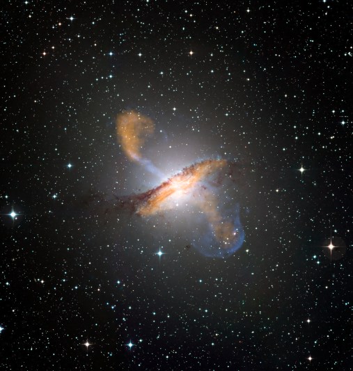 Colour composite image of Centaurus A, revealing the lobes and jets emanating from the active galaxy’s central black hole. This is a composite of images obtained with three instruments, operating at very different wavelengths. The 870-micron submillimetre data, from LABOCA on APEX, are shown in orange. X-ray data from the Chandra X-ray Observatory are shown in blue. Visible light data from the Wide Field Imager (WFI) on the MPG/ESO 2.2 m telescope located at La Silla, Chile, show the stars and the galaxy’s characteristic dust lane in close to